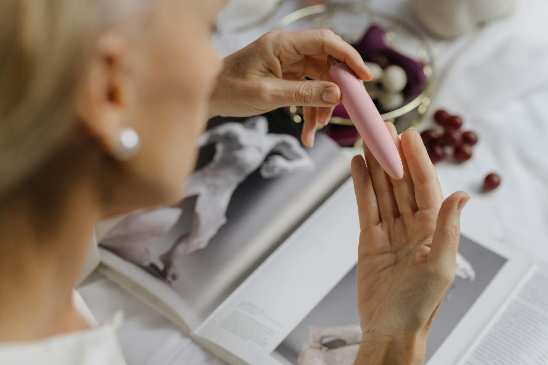 Close-up of a person holding a pink vibrator with books nearby, emphasizing personal pleasure and intimate self-discovery